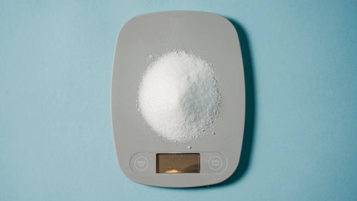 Top view of kitchen scales with electronic display measuring weight of sugar on blue background